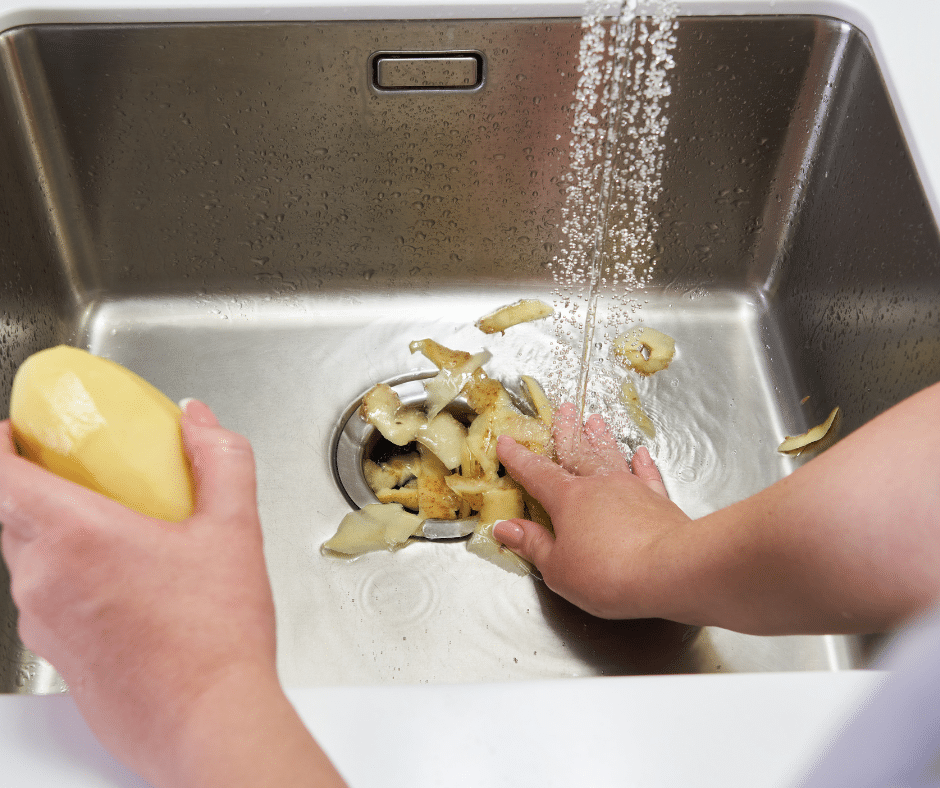 A person places potato peels down a garbage disposal 