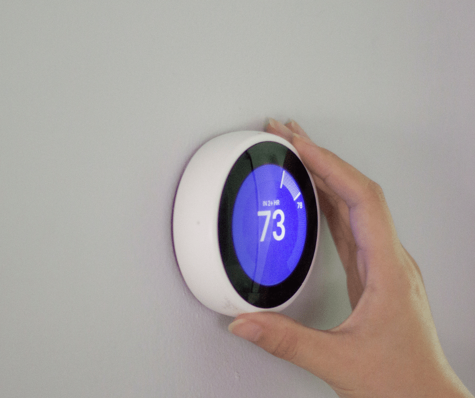 A person controls a smart thermostat, setting it to 73 degrees