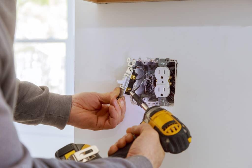 Electrician installing an outlet and switch with a power drill.